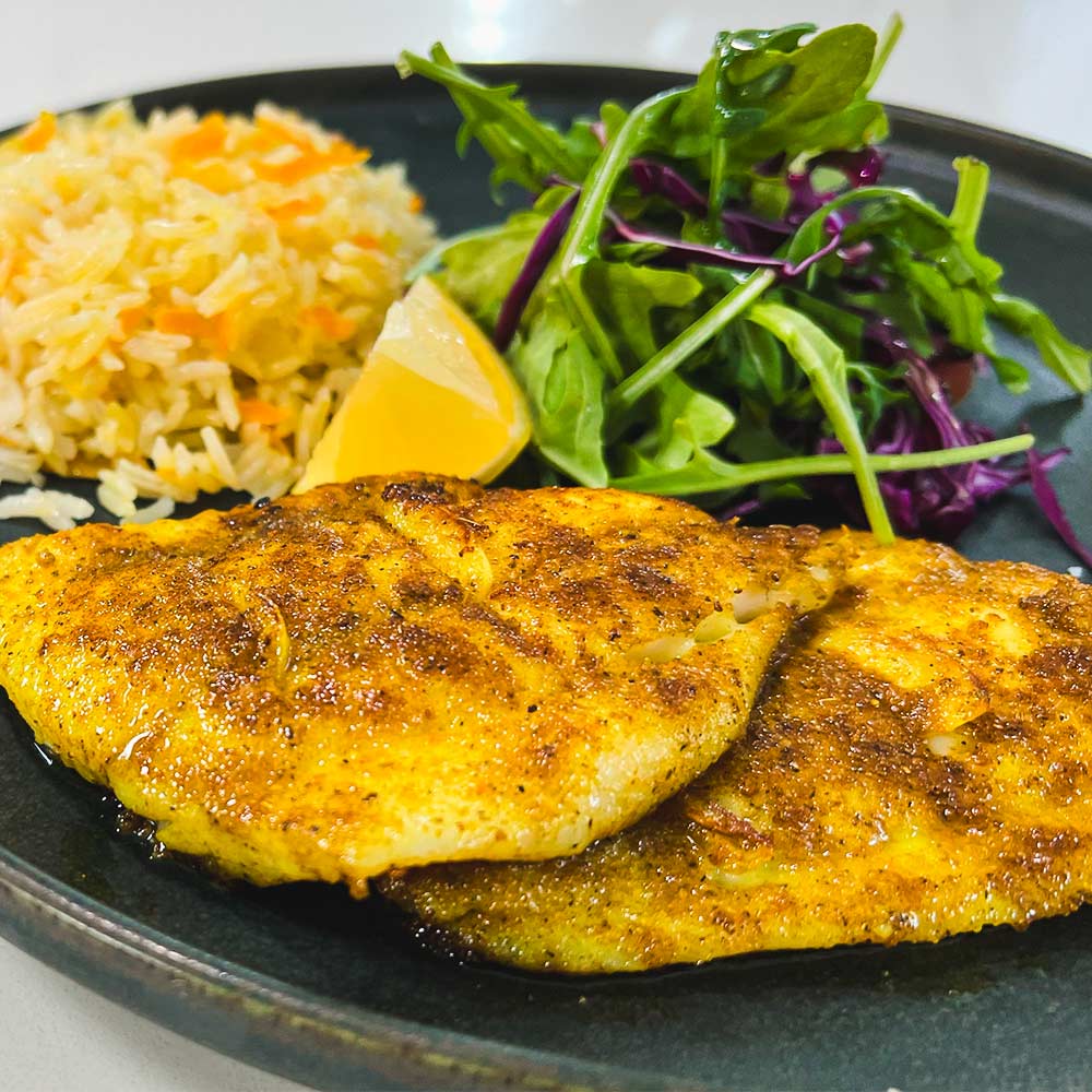 A plate with two fish fillets seared with yellow Mediterranean spice blend "Fish Outta Water". On a gray plate served with perfect rice made with onion and grated carrot, and green salad.