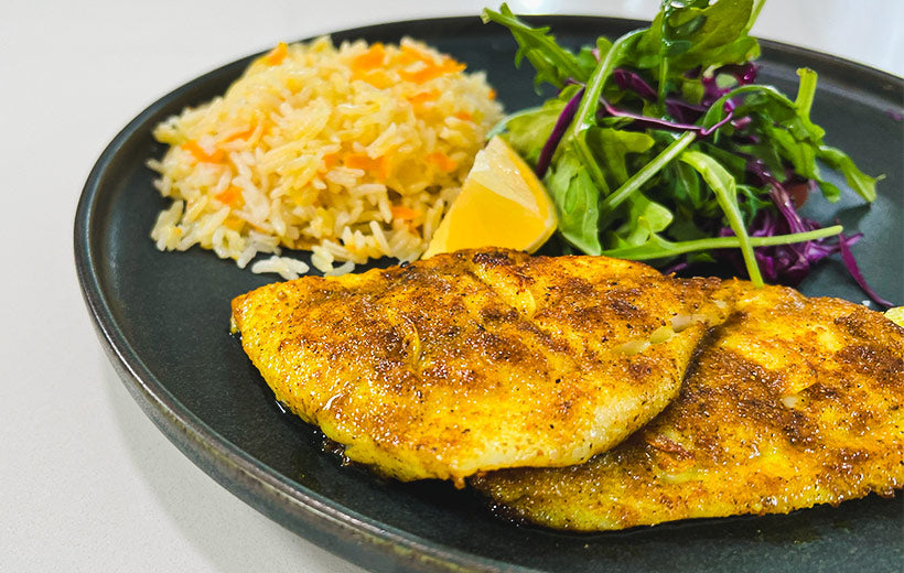 A plate with two fish fillets seared with yellow Mediterranean spice blend "Fish Outta Water". On a gray plate served with perfect rice made with onion and grated carrot, and green salad.