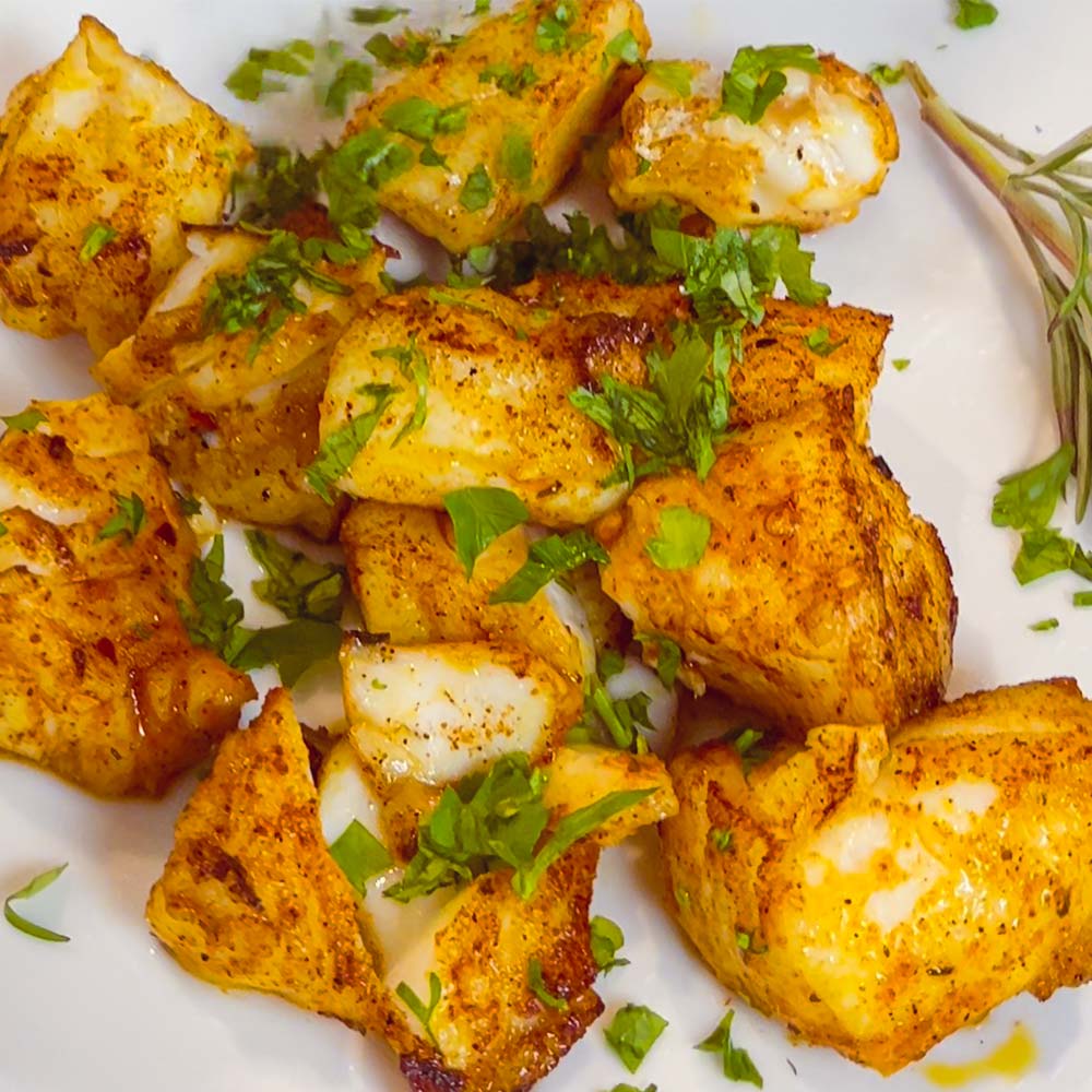 Fish bites, pan-seared with mediterranean spice blend "Grill-Thrill". On a plate garnished with chopped herbs.