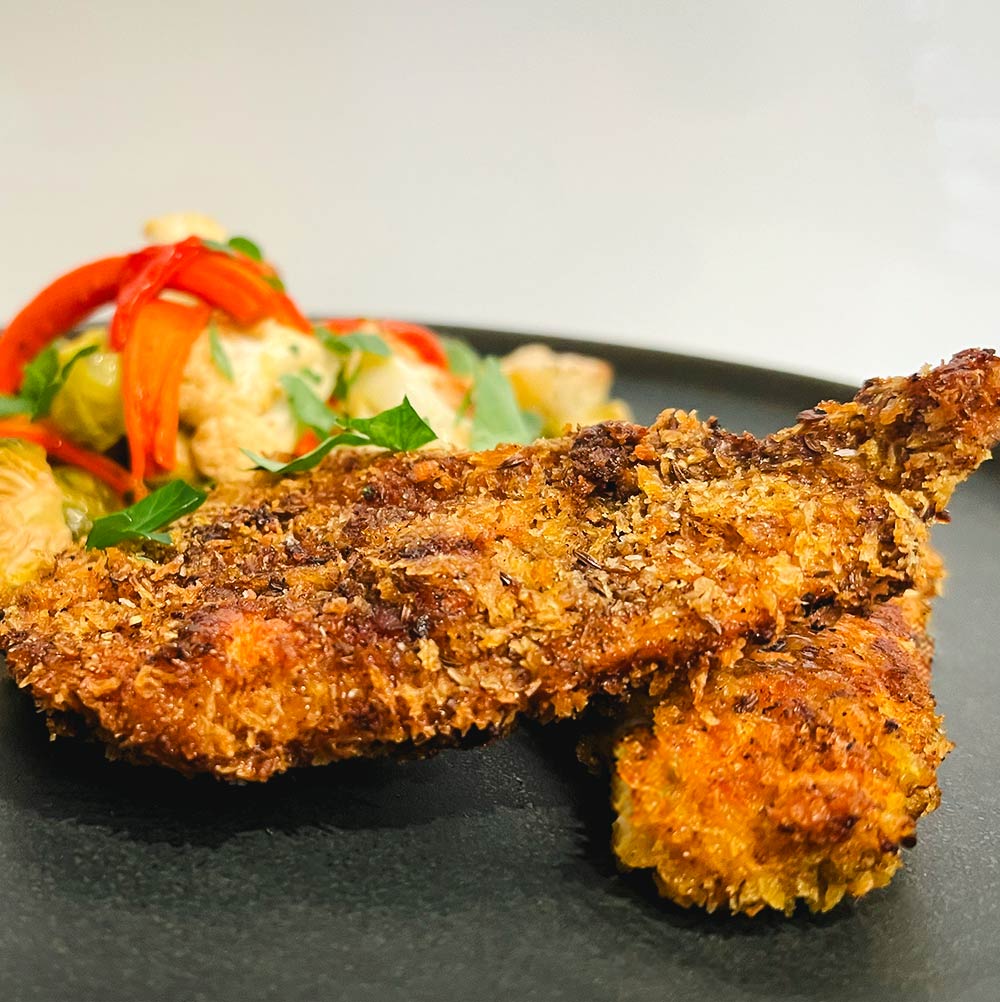 A plate with two pieces of perfect Schnitzel made with Mediterranean "Schnitz'em" spice blend. Next to it, colorful roasted vegetables.